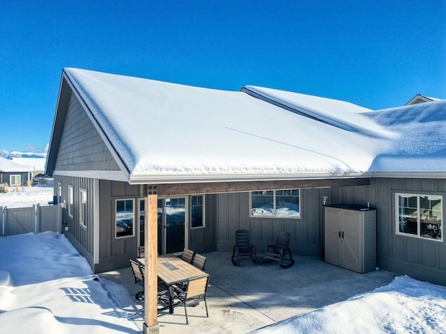 snow covered rear of property with board and batten siding, a patio, and fence