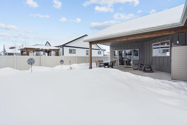 snow covered rear of property featuring board and batten siding and fence private yard