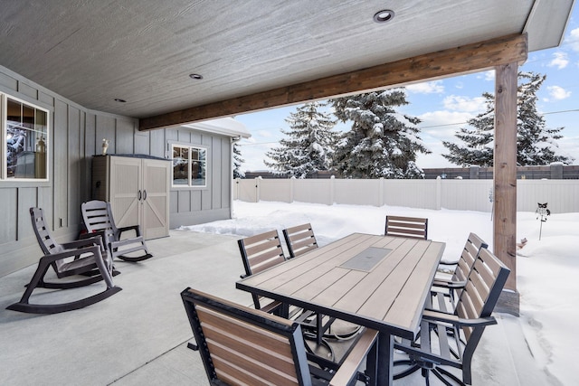 snow covered patio featuring outdoor dining area and a fenced backyard