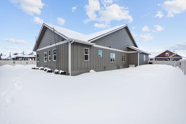 view of snow covered exterior with fence and board and batten siding