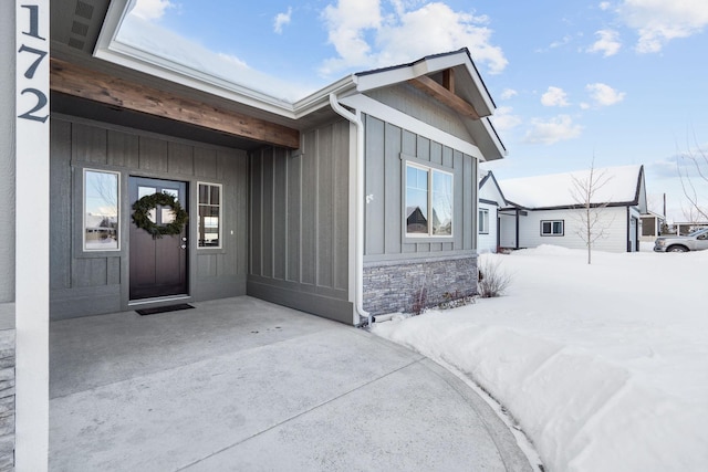 snow covered property entrance with board and batten siding and stone siding