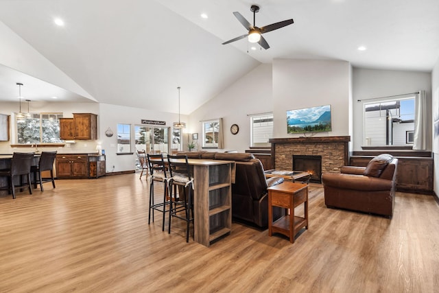 living area featuring a healthy amount of sunlight, light wood finished floors, a fireplace, and high vaulted ceiling