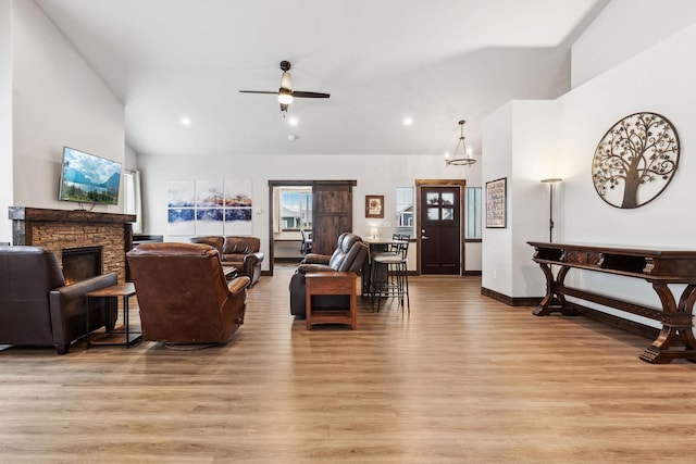 living area with light wood-style floors, ceiling fan, a stone fireplace, and high vaulted ceiling