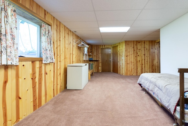 carpeted bedroom featuring wood walls, white fridge, and a paneled ceiling