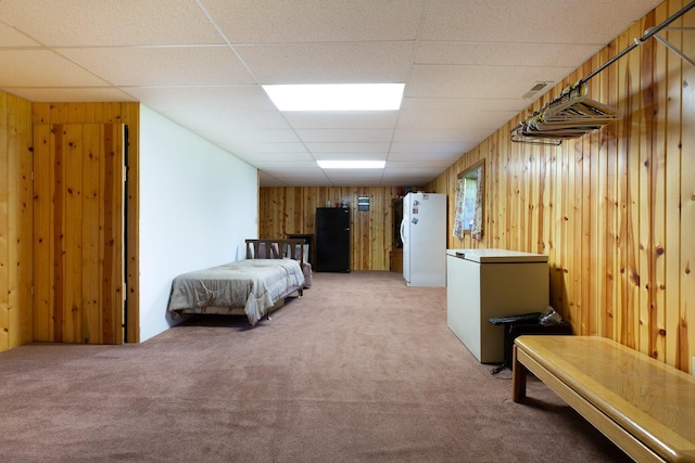 bedroom featuring wood walls, carpet, freestanding refrigerator, and refrigerator