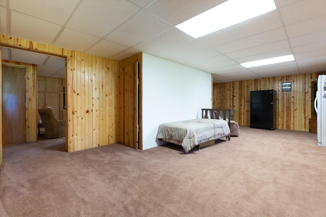 bedroom featuring freestanding refrigerator, a drop ceiling, wood walls, and carpet