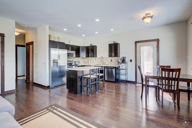 kitchen with a breakfast bar area, stainless steel appliances, a kitchen island, light countertops, and backsplash