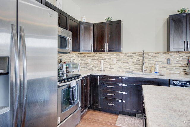 kitchen featuring light wood-type flooring, decorative backsplash, stainless steel appliances, and a sink