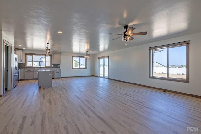 kitchen with light wood-style flooring, open floor plan, backsplash, freestanding refrigerator, and a center island