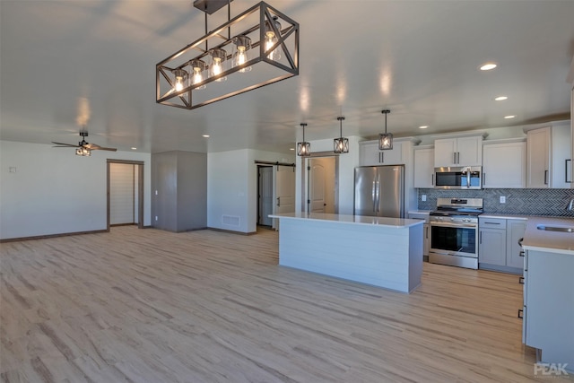 kitchen with a kitchen island, appliances with stainless steel finishes, open floor plan, decorative light fixtures, and light countertops