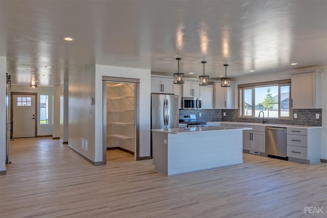 kitchen featuring light wood-style flooring, hanging light fixtures, appliances with stainless steel finishes, light countertops, and a center island