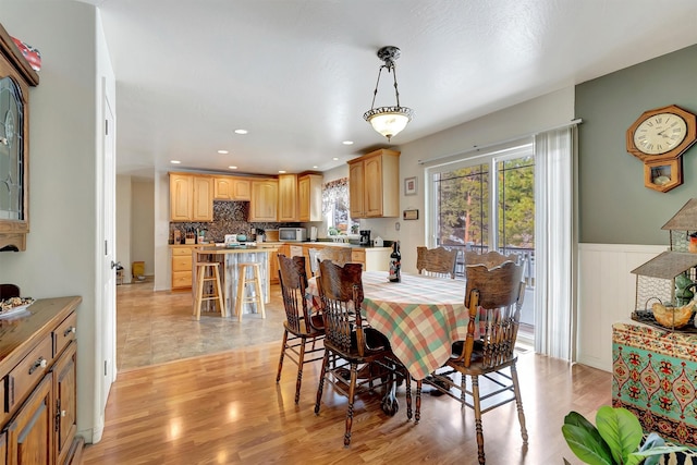 dining room with light wood-type flooring, a wainscoted wall, a healthy amount of sunlight, and recessed lighting