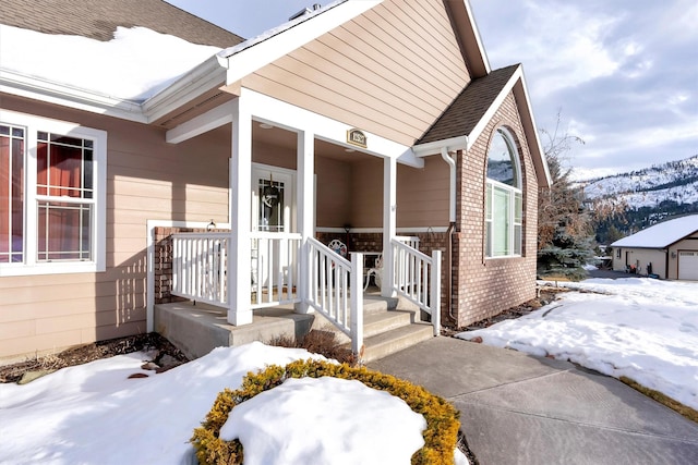 snow covered property entrance featuring roof with shingles, a mountain view, and brick siding