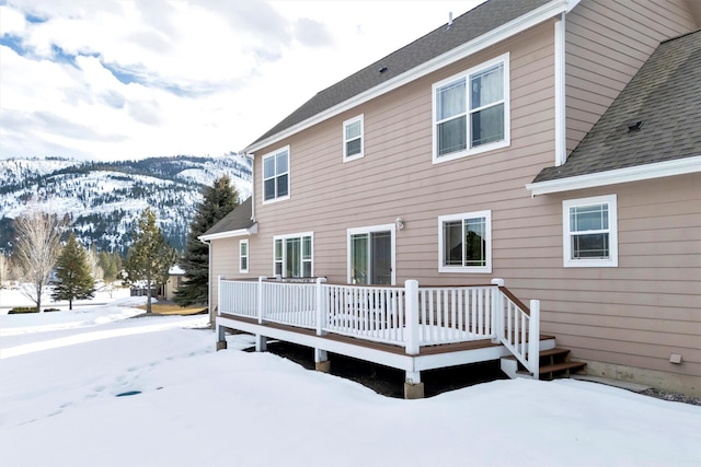 snow covered house featuring a deck and roof with shingles