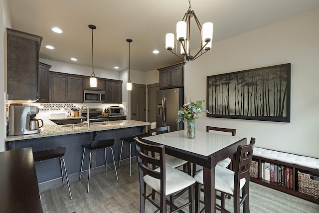 kitchen featuring light stone counters, a sink, dark brown cabinets, appliances with stainless steel finishes, and pendant lighting