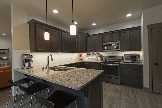 kitchen with dark brown cabinetry, appliances with stainless steel finishes, decorative light fixtures, a peninsula, and a sink