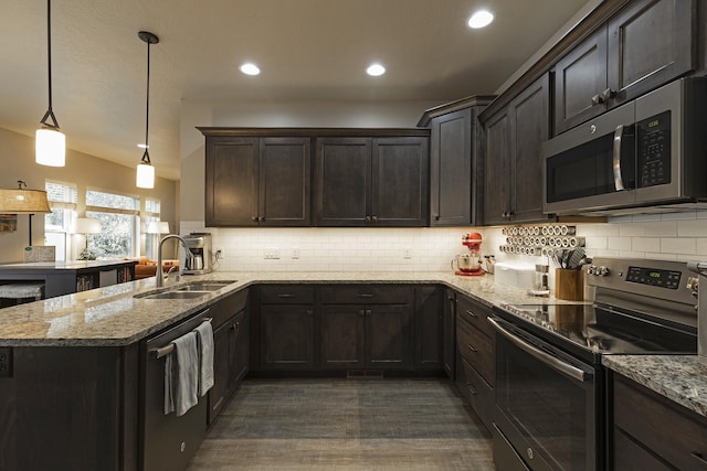 kitchen featuring a peninsula, light stone countertops, appliances with stainless steel finishes, and pendant lighting