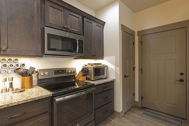 kitchen with dark brown cabinets, appliances with stainless steel finishes, backsplash, and light stone counters