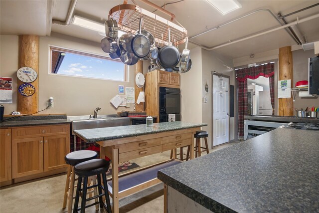 kitchen featuring dobule oven black, dark countertops, a kitchen island, a breakfast bar area, and a sink