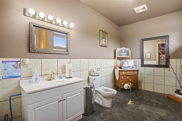 bathroom featuring concrete flooring, toilet, vanity, visible vents, and tile walls