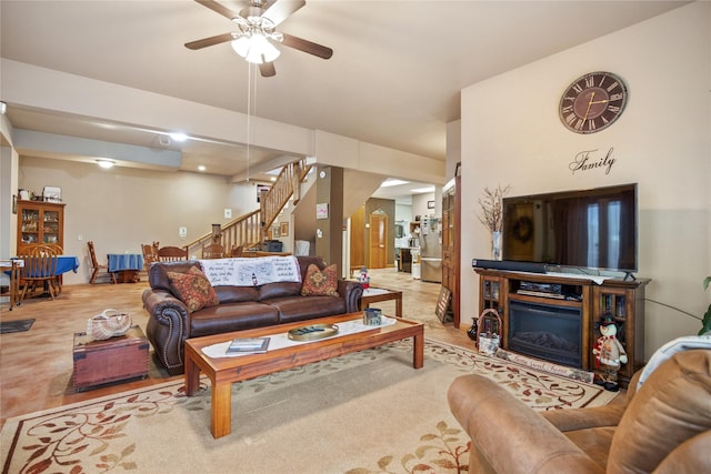 living area with stairs, a glass covered fireplace, and a ceiling fan