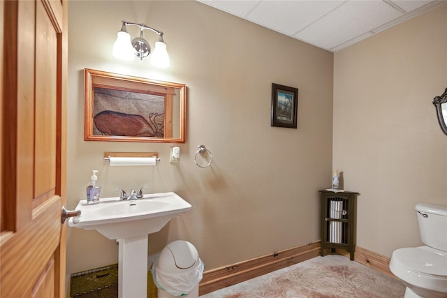 half bath featuring toilet, baseboards, and a sink