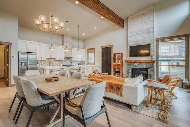 dining room featuring light wood-style floors, high vaulted ceiling, beamed ceiling, and a stone fireplace