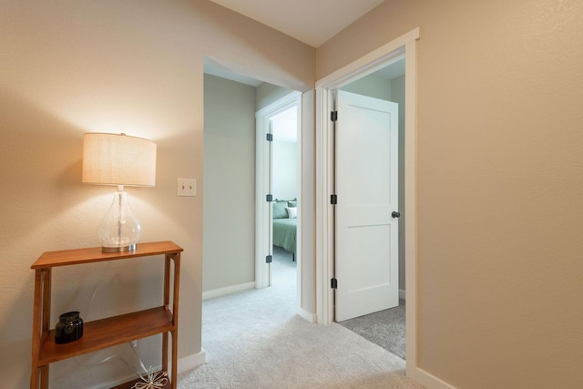 hallway with baseboards and light colored carpet