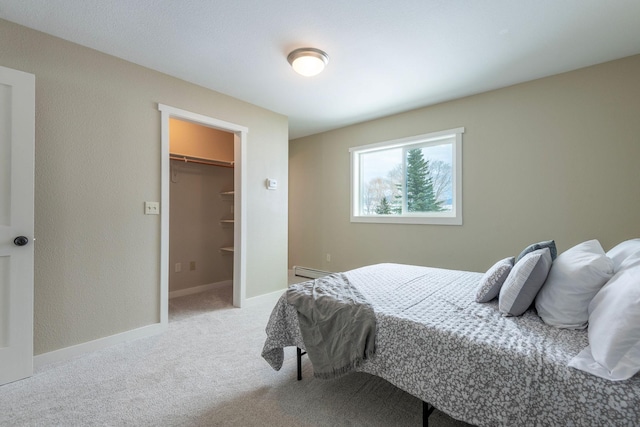 bedroom featuring a walk in closet, baseboards, baseboard heating, and carpet flooring