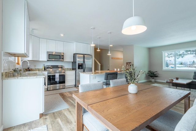 kitchen featuring hanging light fixtures, appliances with stainless steel finishes, white cabinets, a sink, and a kitchen island