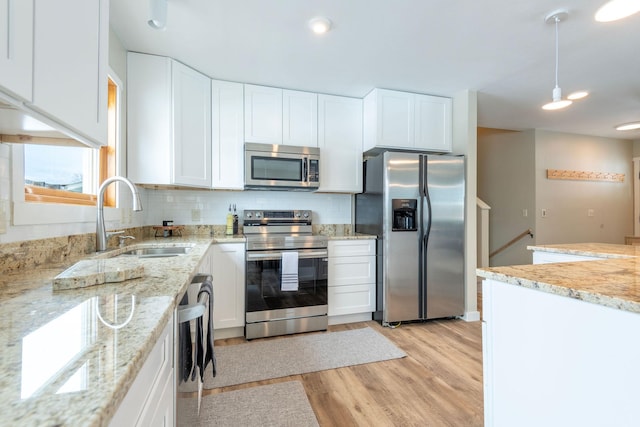 kitchen with appliances with stainless steel finishes, white cabinets, a sink, and light stone counters