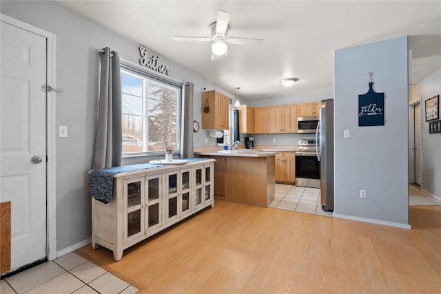 kitchen with appliances with stainless steel finishes, decorative light fixtures, light countertops, light brown cabinetry, and light wood-style floors