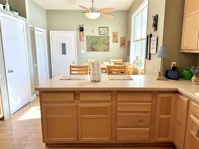 kitchen featuring a peninsula, light wood finished floors, light countertops, and a ceiling fan