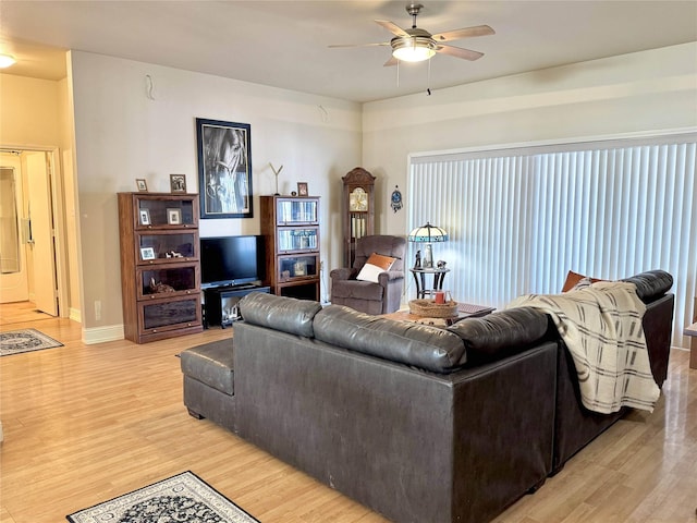 living area with light wood-style flooring, baseboards, and a ceiling fan