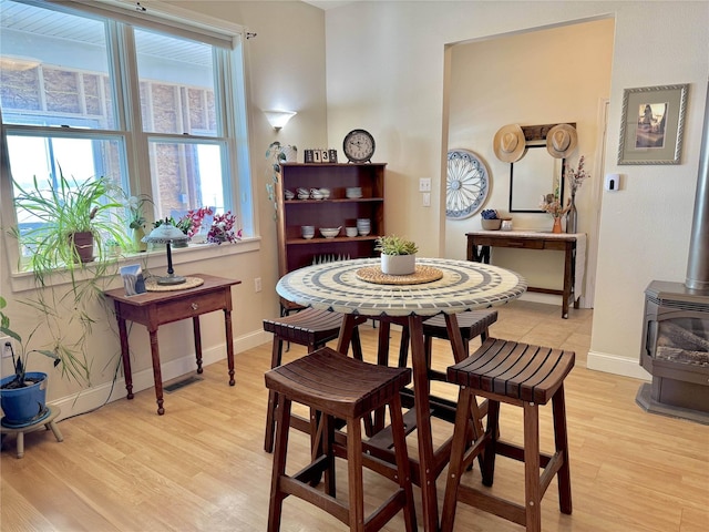 dining room with a wood stove, baseboards, visible vents, and light wood finished floors