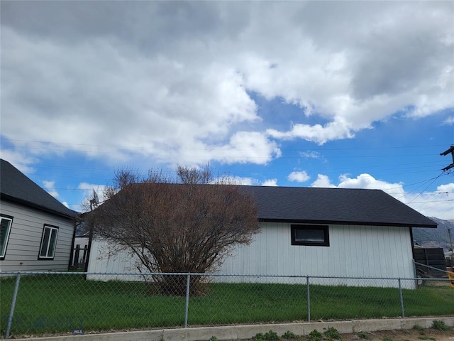 view of property exterior featuring a yard, a shingled roof, and fence