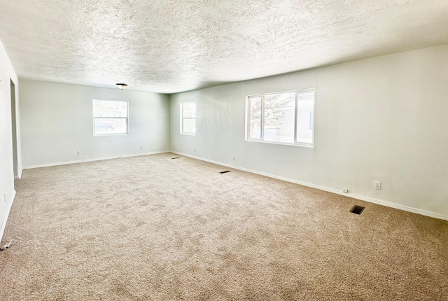 carpeted spare room with a textured ceiling, visible vents, and baseboards