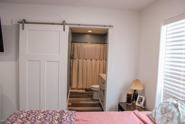 bedroom featuring ensuite bathroom, a barn door, and dark wood finished floors