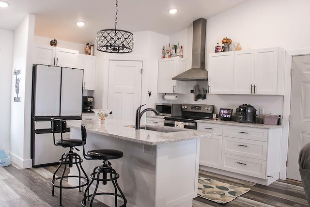 kitchen featuring pendant lighting, appliances with stainless steel finishes, white cabinetry, an island with sink, and wall chimney exhaust hood