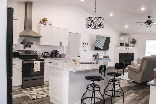 kitchen featuring wall chimney exhaust hood, decorative light fixtures, a center island with sink, and electric stove