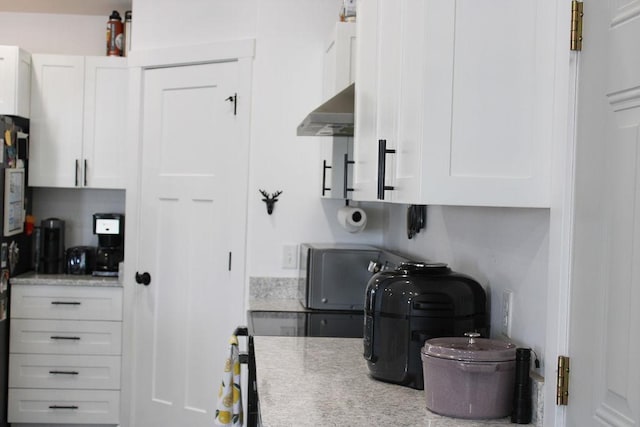 kitchen featuring light countertops, wall chimney range hood, and white cabinetry