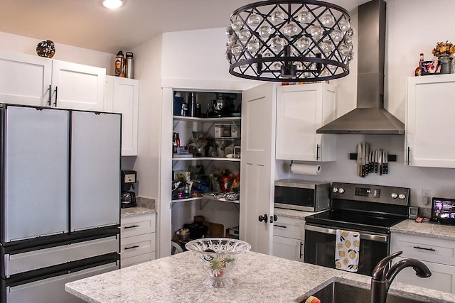 kitchen featuring light stone counters, appliances with stainless steel finishes, white cabinetry, a sink, and wall chimney range hood