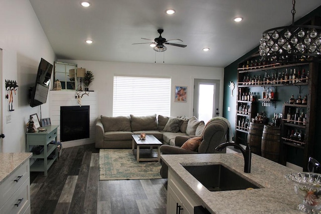 living room with a fireplace, a ceiling fan, vaulted ceiling, wet bar, and dark wood finished floors