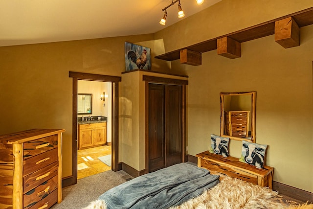 bedroom with lofted ceiling, light carpet, baseboards, and connected bathroom