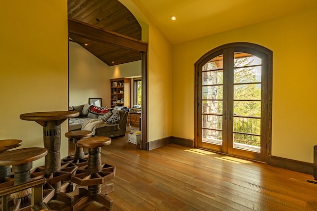 doorway to outside featuring arched walkways, vaulted ceiling, plenty of natural light, and wood finished floors