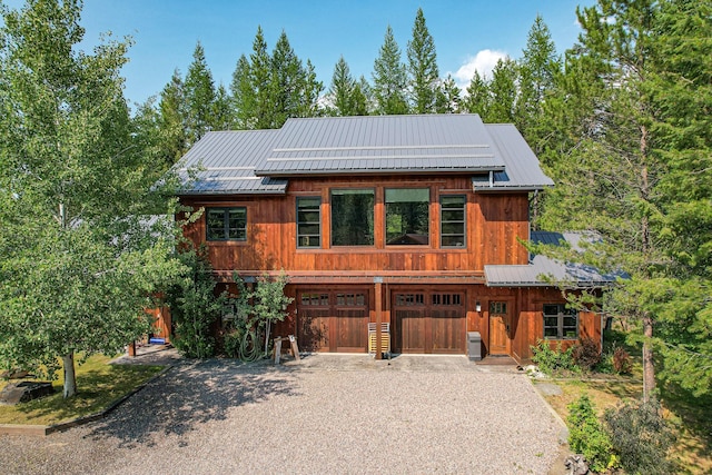 view of front of home featuring driveway, central AC unit, metal roof, an attached garage, and roof mounted solar panels