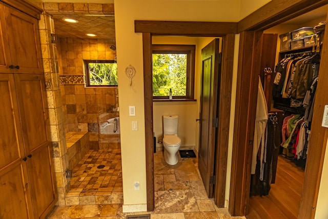 bathroom with a walk in closet, stone tile flooring, toilet, a stall shower, and baseboards