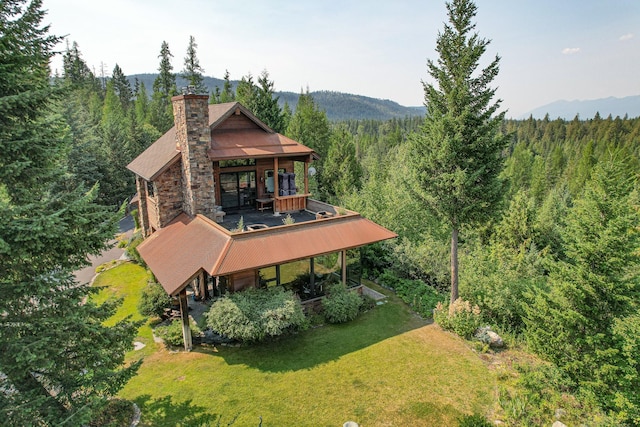 rear view of house with a chimney, a lawn, a mountain view, and a wooded view