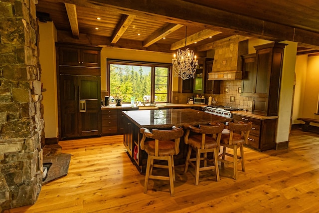 kitchen with tasteful backsplash, custom range hood, a kitchen island, and light wood finished floors