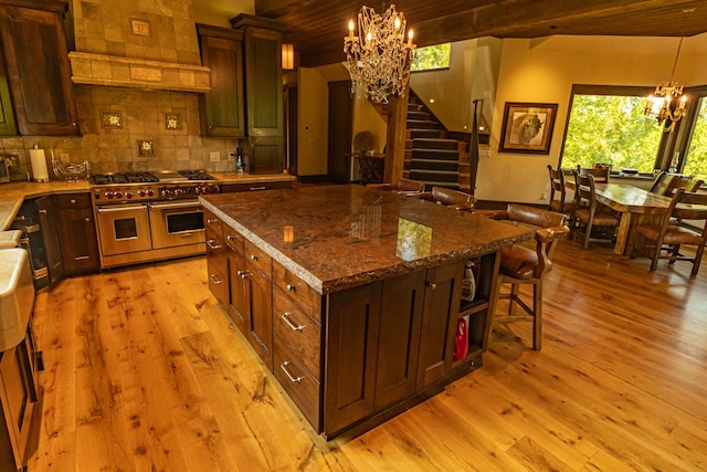 kitchen with dark stone counters, a center island, an inviting chandelier, custom exhaust hood, and double oven range